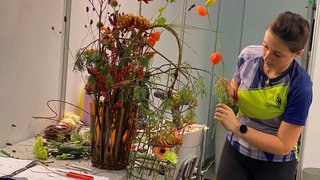© WorldSkill International Frau arrangiert bunte Blumen in Vase auf Tisch in einem Raum