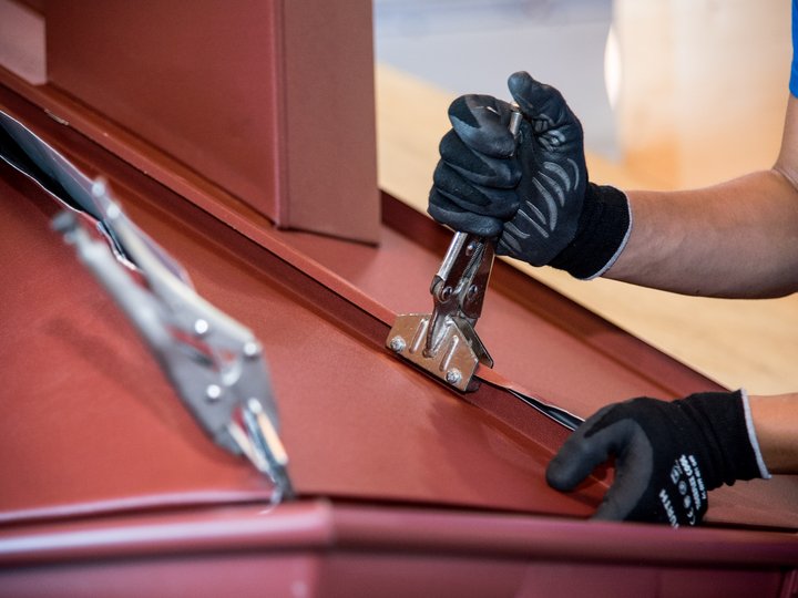 Lattonieri edili e artistici Mano di operaio ripara tetto metallico rosso con pinza e vite