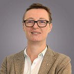 Das lvh-Team Porträt einer Person mit Brille und braunem Blazer vor grauem Hintergrund