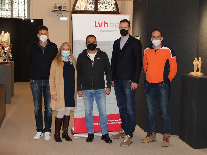 Artigianato Artistico della Val Gardena TRA(dition)art Cinque persone con mascherine davanti a uno striscione lvhap in una galleria