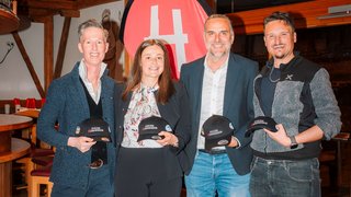 News Quattro persone tengono cappellini Stolzer Handwerker davanti a uno striscione rosso