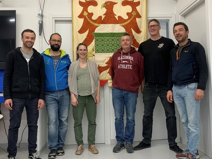 Impegnati per il futuro dell'artigianato della stufa Sei persone in piedi davanti a uno stemma con un'aquila in una stanza