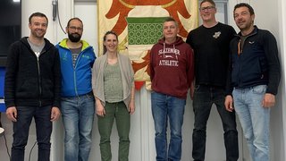 News Sechs Personen stehen vor einem Wappen mit Adler in einem Raum