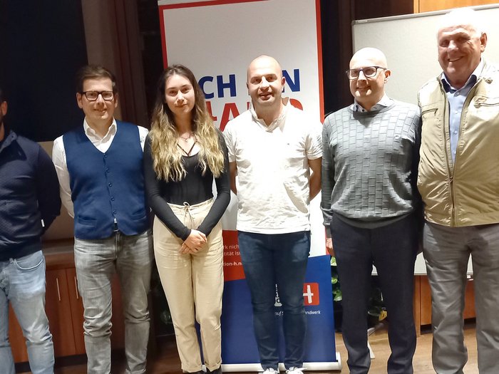 Handwerk: Innovativ. Leistungsstark. Nachhaltig Sechs Personen stehen vor einer Werbetafel in einem Raum