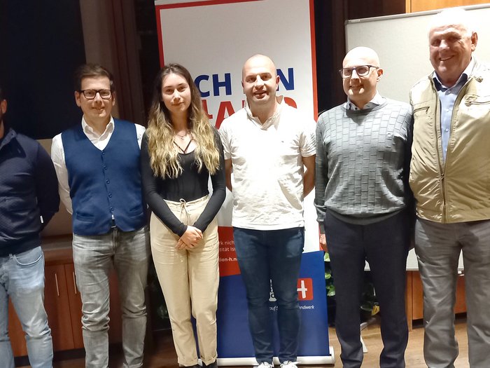 Handwerk: Innovativ. Leistungsstark. Nachhaltig Sechs Personen stehen vor einer Werbetafel in einem Raum