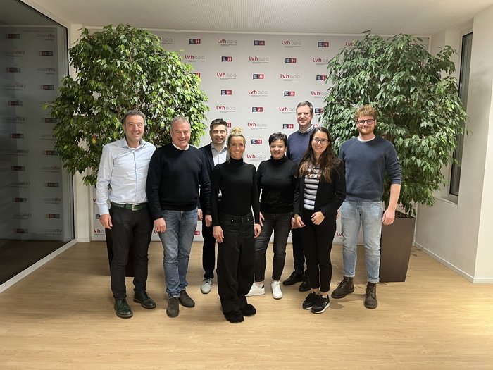 Neue lvh-Arbeitsgruppe gestaltet die Zukunft der Berufsbildung aktiv mit Gruppenfoto von acht Personen vor einer LVH-APA-Wand mit grünen Pflanzen
