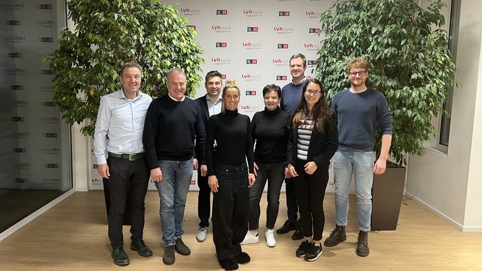 Neue lvh-Arbeitsgruppe gestaltet die Zukunft der Berufsbildung aktiv mit Gruppenfoto von acht Personen vor einer LVH-APA-Wand mit grünen Pflanzen