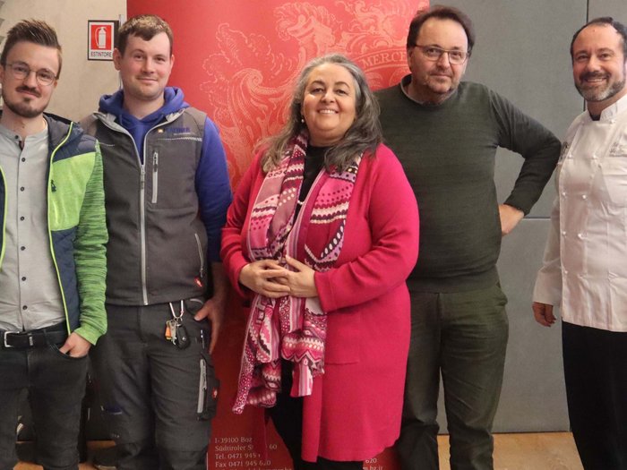 10. Wirtschaftstag für Berufsschüler/innen: eine praxisnahe Vorbereitung auf den Berufseinstieg Fünf lächelnde Personen vor roter Wand, eine trägt Kochjacke