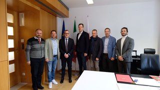 News Sieben Männer in einem Büro vor drei Flaggen stehen zusammen