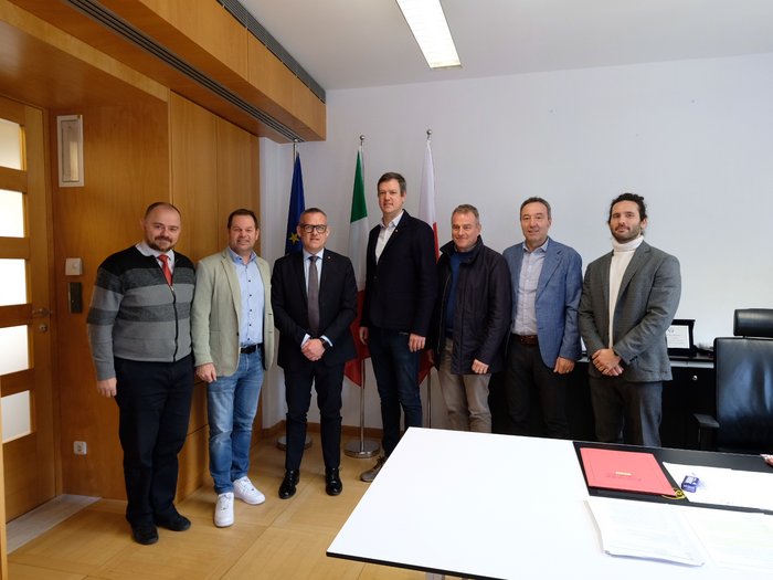 Impostare la rotta per il futuro: i vertici di lvh.apa incontrano l’assessore Bianchi Sette uomini in ufficio davanti a tre bandiere in piedi insieme