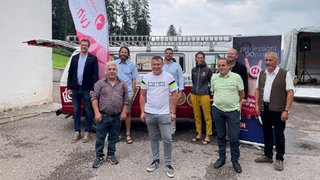 News Gruppenfoto von neun Personen vor Fahnen und einem Anhänger im Freien