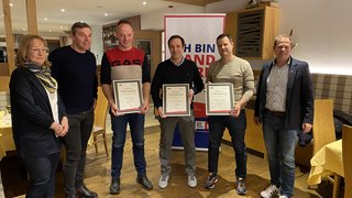 News Sieben Personen stehen, drei halten Urkunden für eine Ehrung in einem Raum