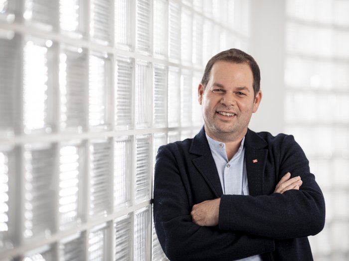 Förderung von arbeitswilligen Pensionisten Mann lehnt lächelnd vor einer Glaswand mit verschränkten Armen