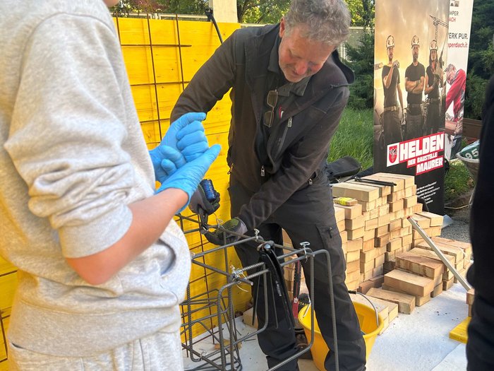 SkillsDay in Lana: Schüler/innen erleben Handwerk hautnah Mann zeigt Jugendlichen Bauarbeit mit Eisenverstärkung und Holz im Hintergrund