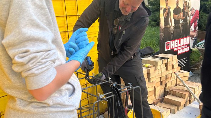 SkillsDay in Lana: Schüler/innen erleben Handwerk hautnah Mann zeigt Jugendlichen Bauarbeit mit Eisenverstärkung und Holz im Hintergrund