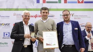 © FGHA / Reiner Zensen Drei Männer bei der Verleihung einer Urkunde und Medaille bei Europameisterschaft Holzbau