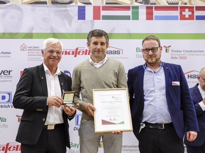 © FGHA / Reiner Zensen Drei Männer bei der Verleihung einer Urkunde und Medaille bei Europameisterschaft Holzbau