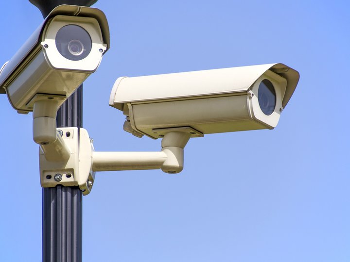 Fakten zum Thema Zwei weiße Überwachungskameras an einem Pfosten vor blauem Himmel
