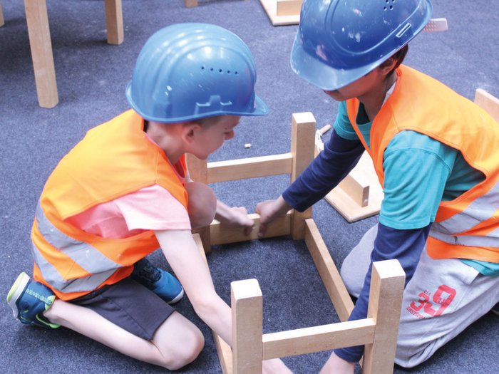 Erlebniswelt Baustelle Zwei Kinder mit Schutzhelmen und Warnwesten bauen ein Holzgestell zusammen