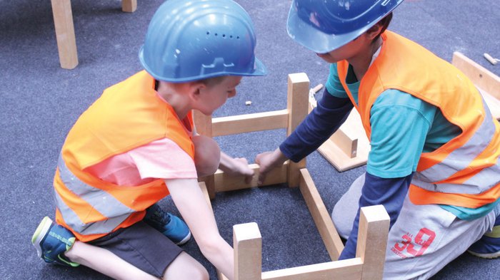 Erlebniswelt Baustelle Zwei Kinder mit Schutzhelmen und Warnwesten bauen ein Holzgestell zusammen