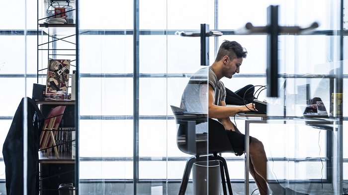 Foto: © Ivo Corrà Mann arbeitet konzentriert an einem Schreibtisch in modernem, hellem Büro
