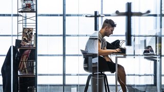 Foto: © Ivo Corrà Mann arbeitet konzentriert an einem Schreibtisch in modernem, hellem Büro