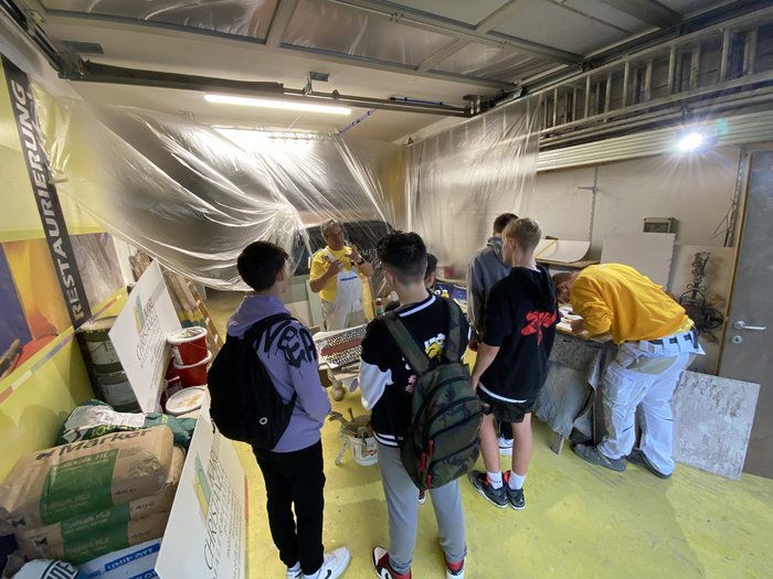 Eine wichtige Entscheidung steht an Gruppe Jugendlicher hört einem Maler in Werkstatt mit Farbeimern und Werkzeug zu