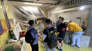 News Gruppe Jugendlicher hört einem Maler in Werkstatt mit Farbeimern und Werkzeug zu