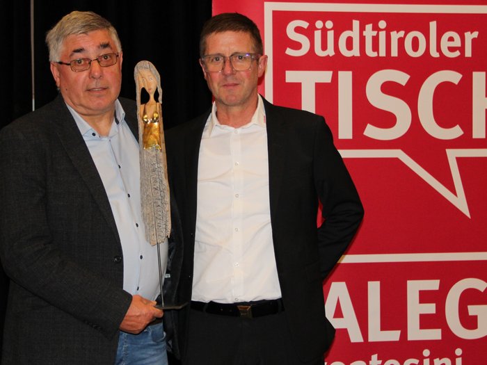 Jahresversammlung der Südtiroler Tischler: Ein Blick auf die Zukunft des Handwerks Zwei Männer mit Trophäe vor rotem Südtiroler Tischler Hintergrund