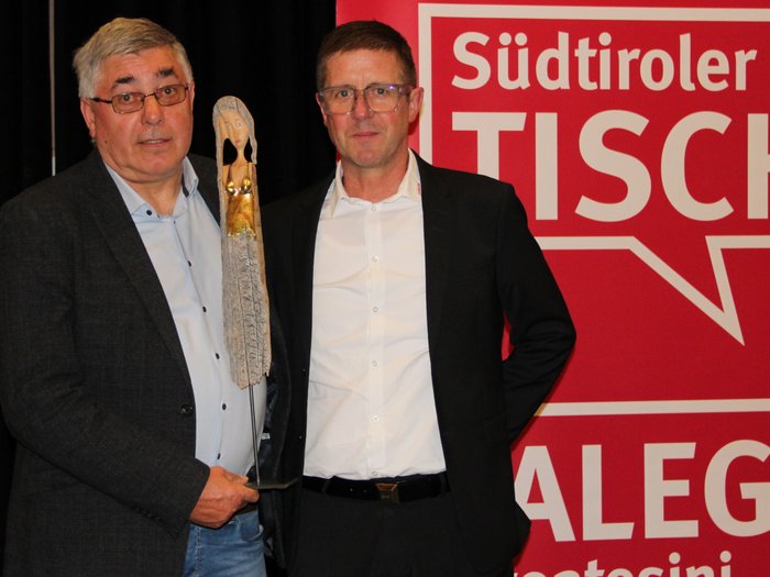 Jahresversammlung der Südtiroler Tischler: Ein Blick auf die Zukunft des Handwerks Zwei Männer mit Trophäe vor rotem Südtiroler Tischler Hintergrund