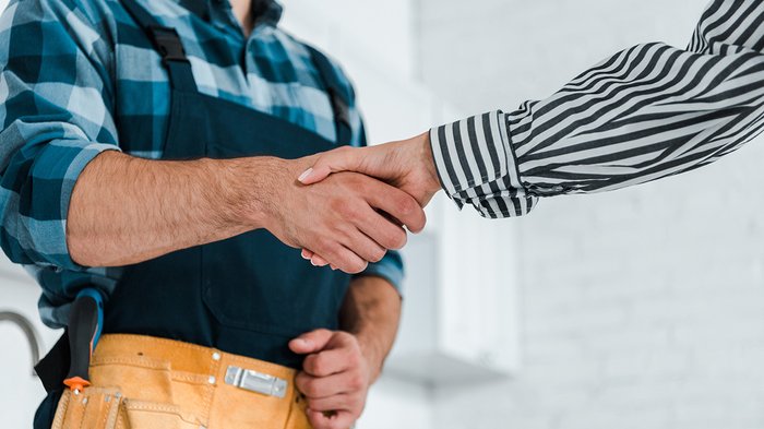 Un servizio che genera fiducia Stretta di mano tra artigiano con cintura degli attrezzi e persona con camicia a righe