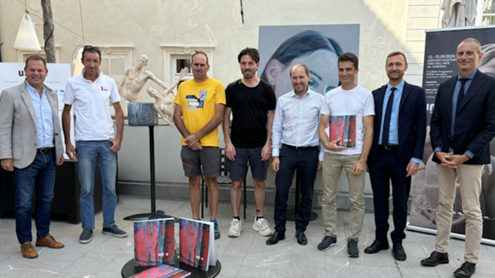 30 Jahre UNIKA Neun Männer stehen vor Skulptur und Gemälde bei Kunstausstellung im Freien