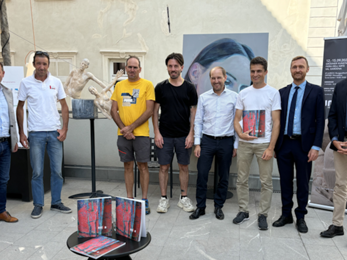 30 Jahre UNIKA Neun Männer stehen vor Skulptur und Gemälde bei Kunstausstellung im Freien