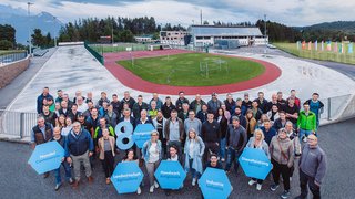 News Große Gruppe von Menschen mit Schildern vor Sportanlage unter bewölktem Himmel
