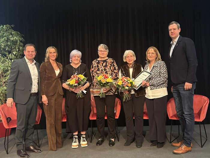 Ricevimento 2025 delle donne nell‘artigianato: “INSIEME creiamo il futuro” Sette persone in piedi su un palco, tre donne con fiori e una con certificato