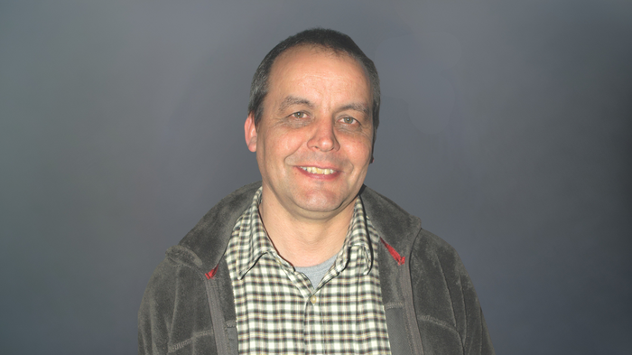 Assemblea annuale condivisa: confronto, innovazione e prospettive chiare Uomo di mezza età con camicia a quadri e giacca sorridente su sfondo grigio