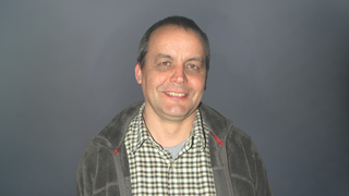 News Mittelalter Mann mit kariertem Hemd und Jacke vor grauem Hintergrund lächelnd