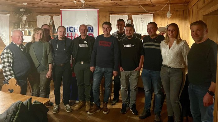 Ulrich Perkmann als Ortsobmann bestätigt Gruppe von elf Personen steht vor Banner in Holzraum