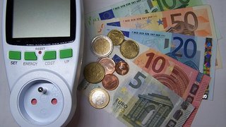 News Energiekostenmessgerät neben Euro-Geldscheinen und Münzen
