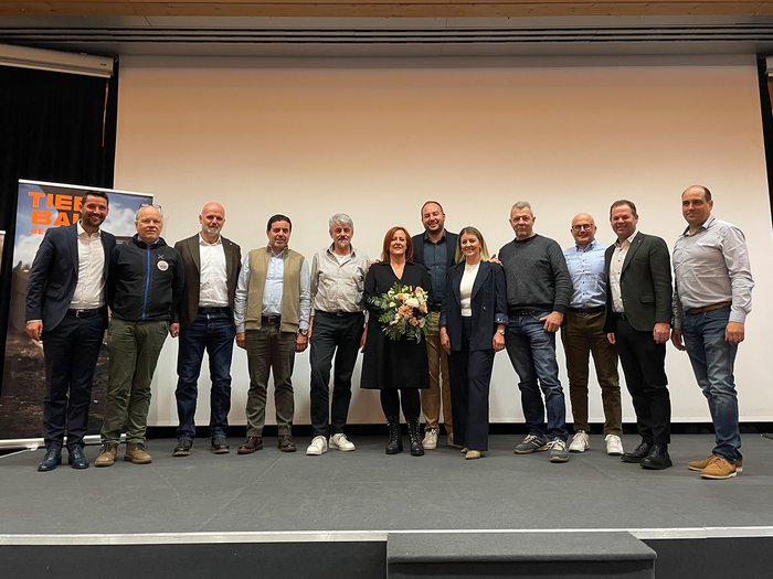 Unsichtbar, aber unverzichtbar: Tiefbauunternehmer/innen setzen starke Akzente Gruppe von elf Personen steht vor weißer Leinwand auf Bühne, eine Frau hält Blumenstrauß