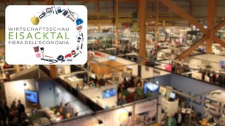 News Messestand mit Wirtschaftsschau Eisacktal Logo und Besuchern in Messehalle