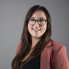 Ansiedlungen und Gewerbeflächen Porträt einer lächelnden Frau mit Brille und brauner Jacke vor grauem Hintergrund