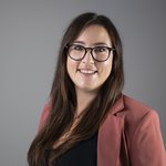 Das lvh-Team Porträt einer lächelnden Frau mit Brille und brauner Jacke vor grauem Hintergrund