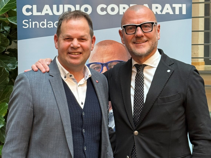 Wirtschaftskompetenz an der Stadtspitze: Claudio Corrarati wird Bürgermeister von Bozen Zwei Männer in Anzügen lächeln vor einem Wahlplakat von Claudio Corzatti