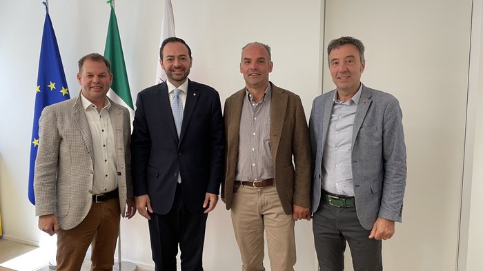 Trasporto merci in Alto Adige: il settore chiede meno burocrazia e migliori condizioni di formazione Quattro uomini in abiti davanti alle bandiere UE, Italia e altre