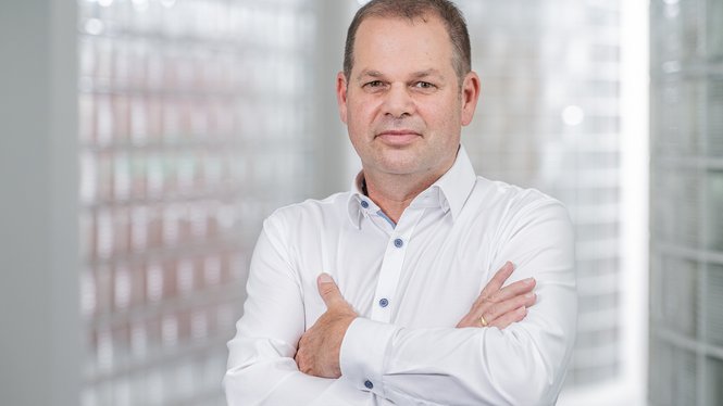 Porträt eines Mannes mit weißem Hemd und verschränkten Armen in hellem Raum