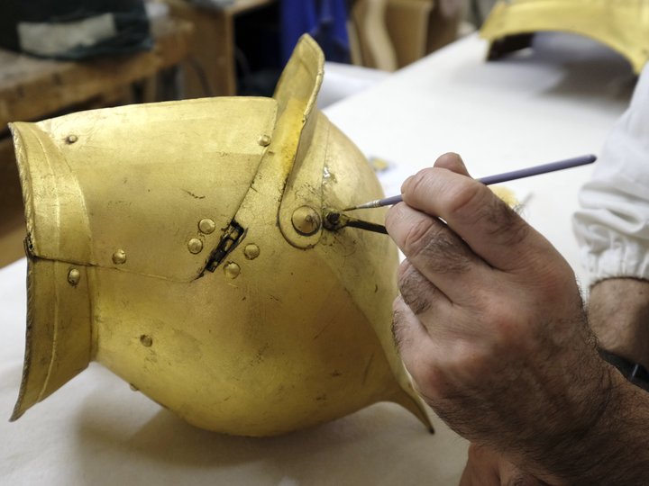 Restauratori Mano che restaura un elmo da cavaliere antico dorato con un pennello