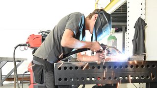 News Arbeiter schweißt Metall in Werkstatt mit Schutzhelm