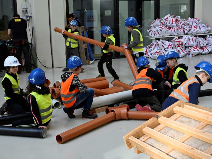 Vivere una giornata in cantiere Bambini con caschi e giubbotti di sicurezza montano tubi grandi al chiuso