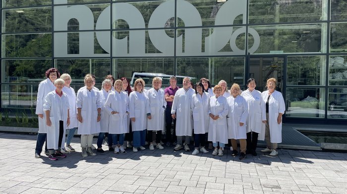 Spunti innovativi per le artigiane dell'Alta Val Pusteria Foto di gruppo di dipendenti con camici bianchi davanti a una grande finestra aziendale